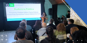 Personas sentadas en sillas mirando a escenario con una pantalla donde se visualiza una presentación y una persona expone.